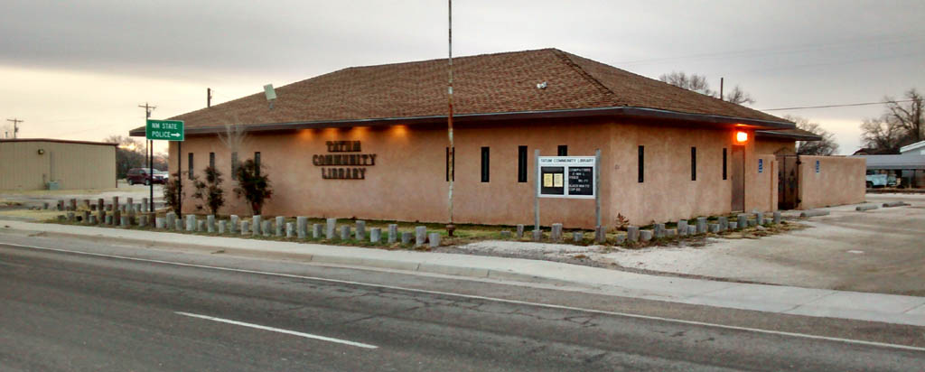 Exterior view of a modest library building with a sign and bulletin board.
